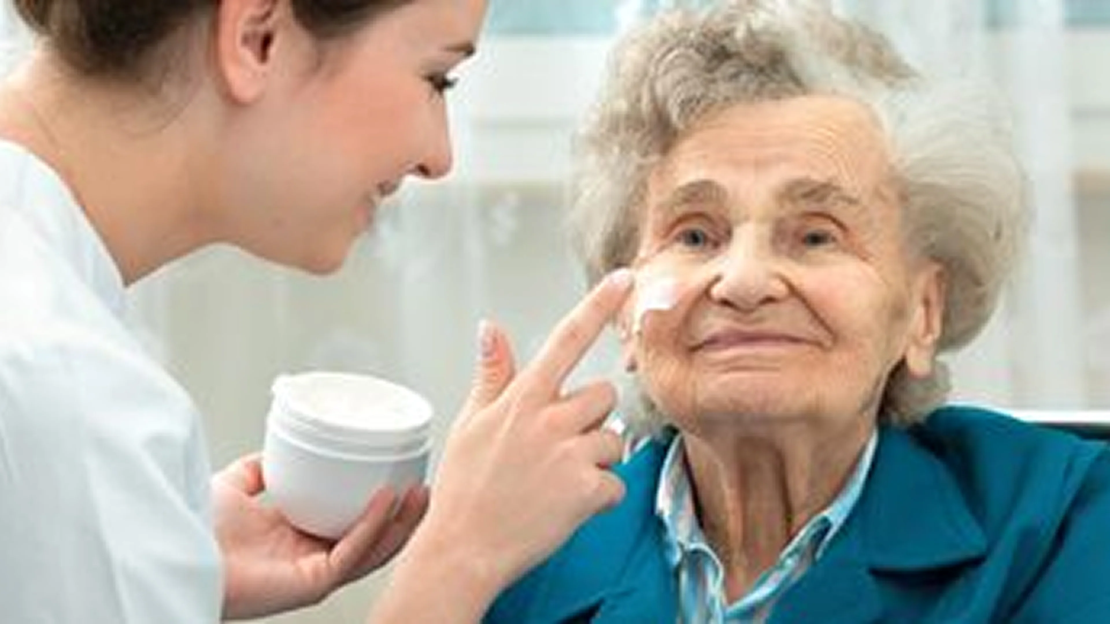 A young woman applying cream on an elderly woman's face.