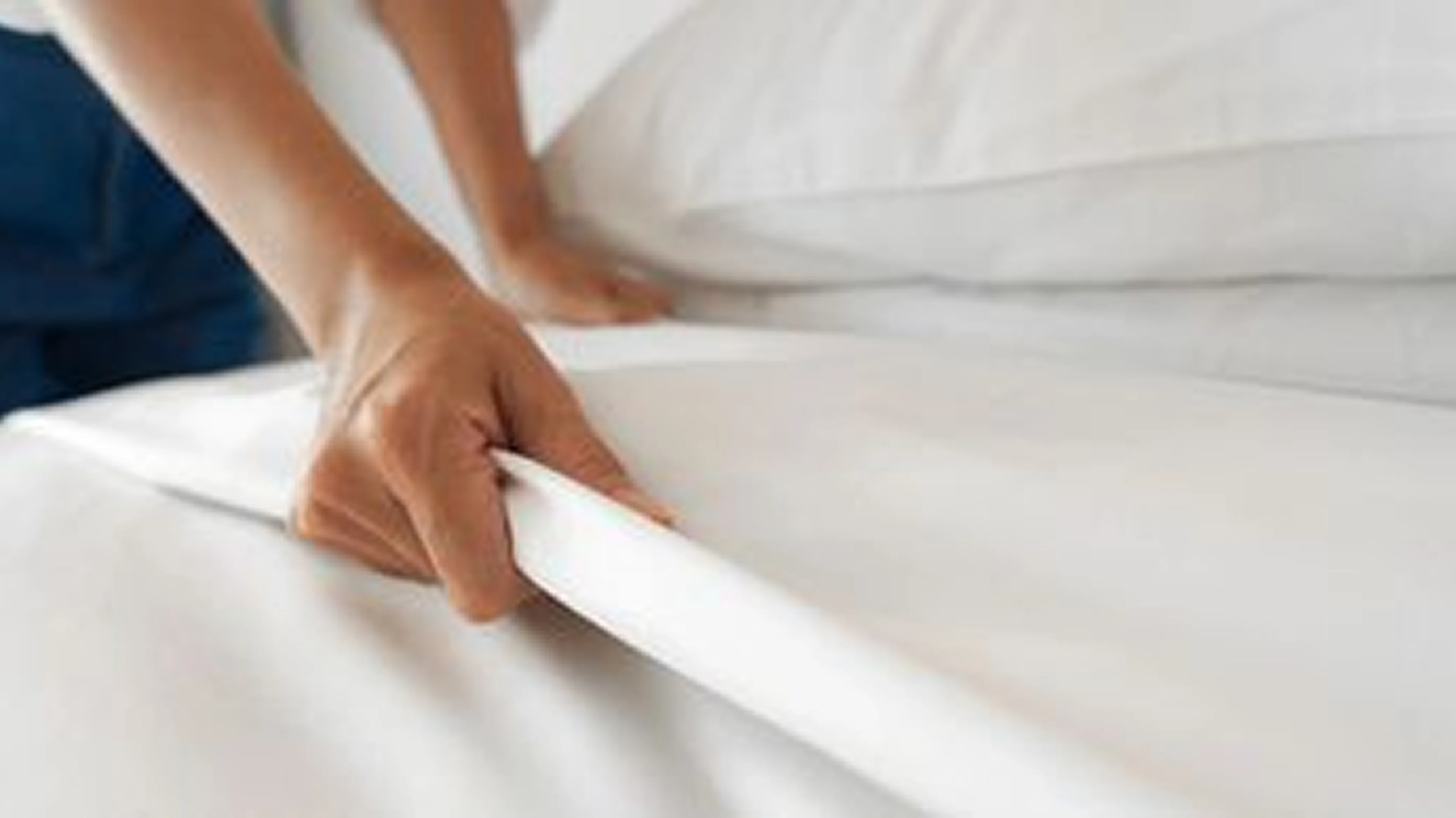 Person pulling a fitted sheet tightly over a mattress.