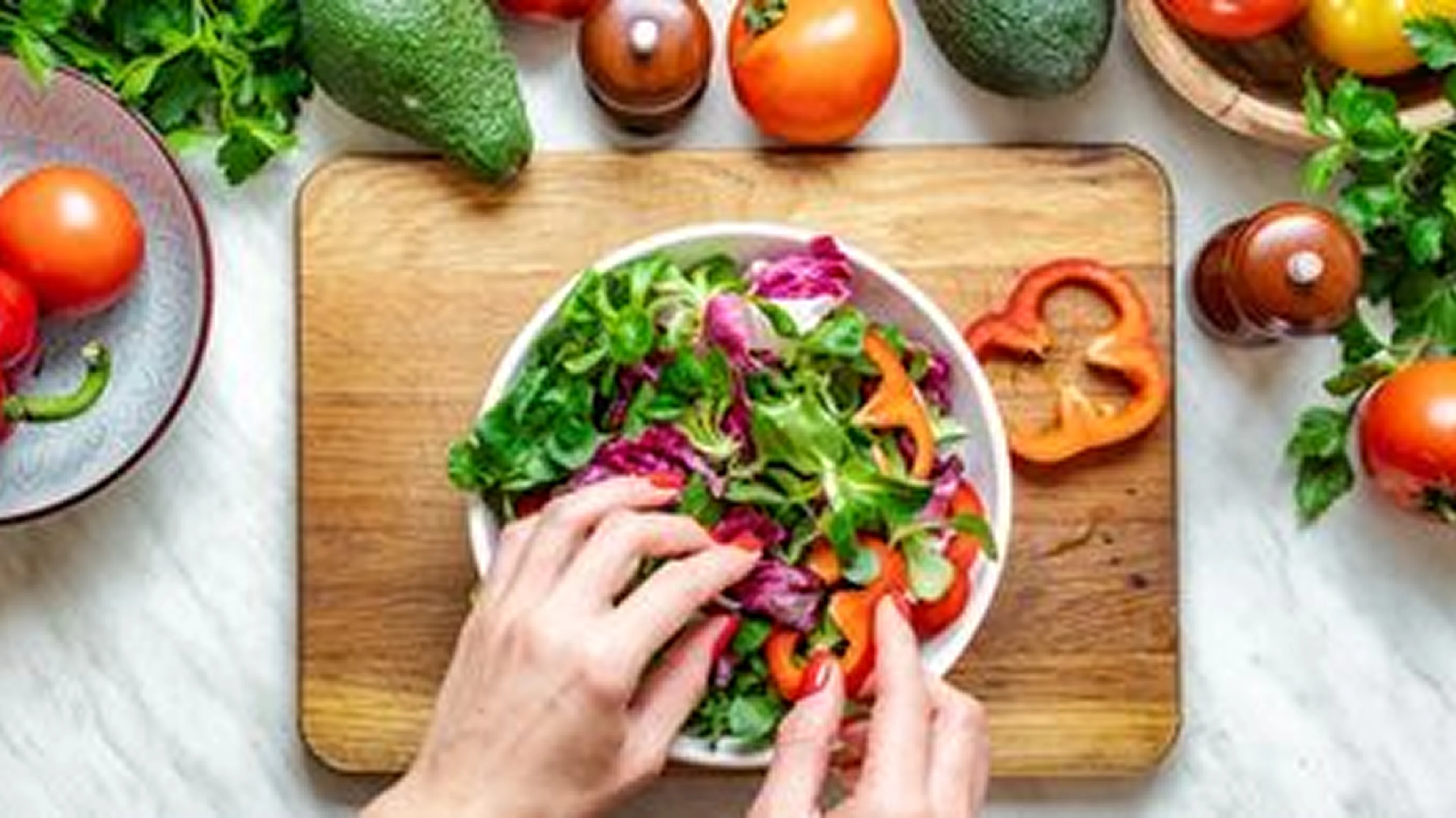 Hands preparing a colorful fresh salad with various veggies on a wooden board.