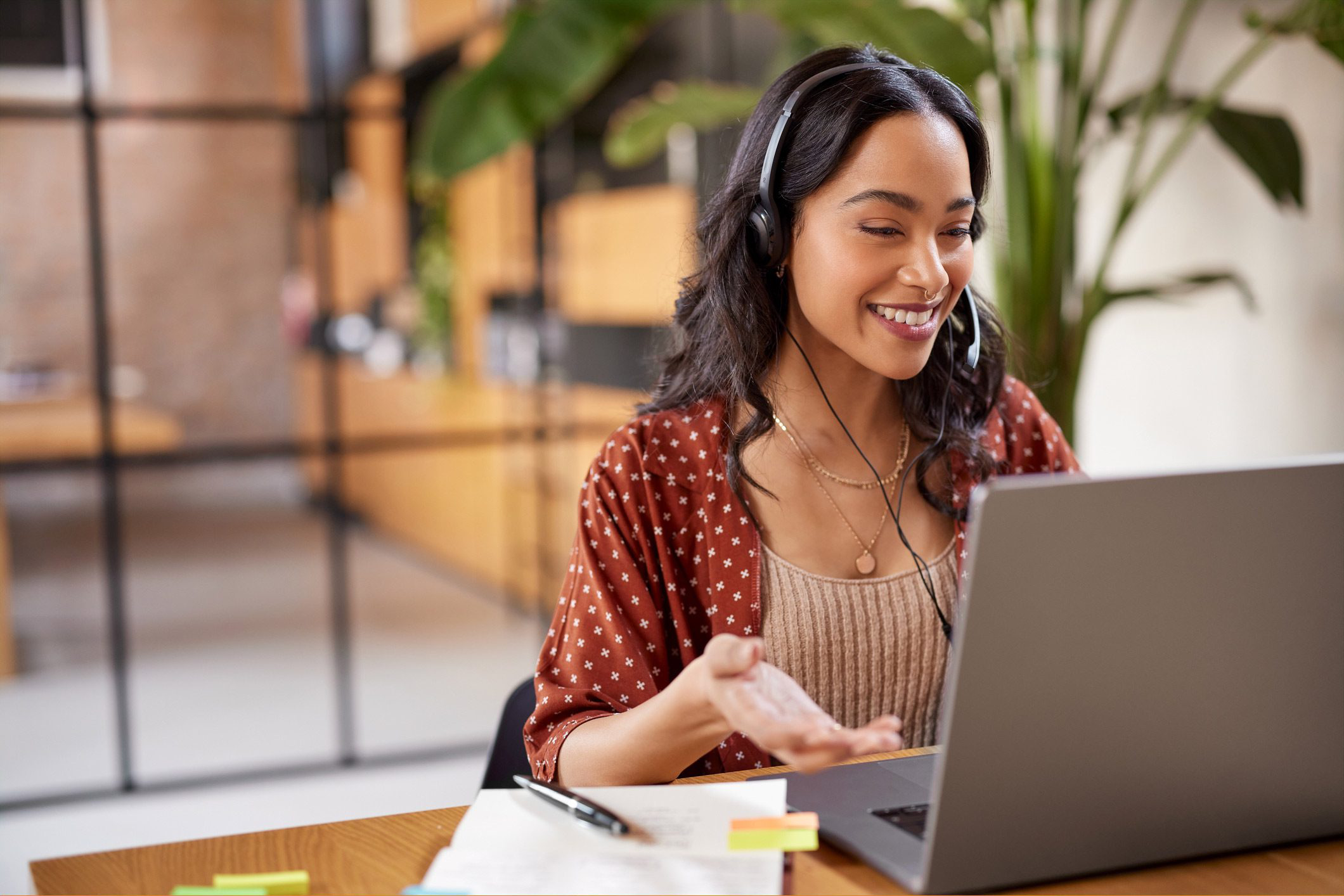 A woman wearing headphones smiling at her laptop in a cozy workspace.